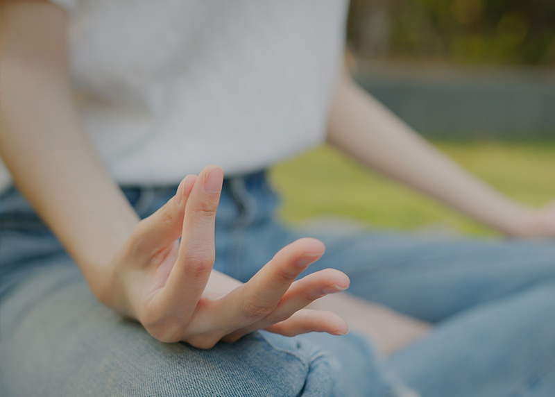 Frau sitzt draussen im Lotussitz, Zeigefinger und Daumen zusammen